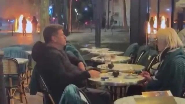 Muškarac i žena uživali u piću i cigareti dok Pariz gori u pozadini